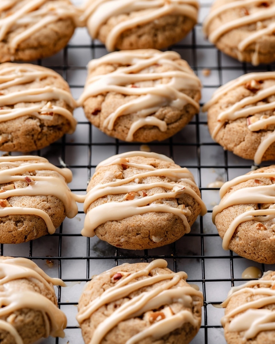 A close-up view shows a batch of soft, round cookies arranged on a black cooling rack over a white marbled surface. Each cookie has a light beige color with visible small bits of nuts inside, and they are generously drizzled with glossy, thick caramel-colored icing. The drizzle varies in shape, some in straight lines and others in swirls, adding texture and shine to the smooth tops of the cookies. Photo taken with an iphone --ar 4:5 --v 7