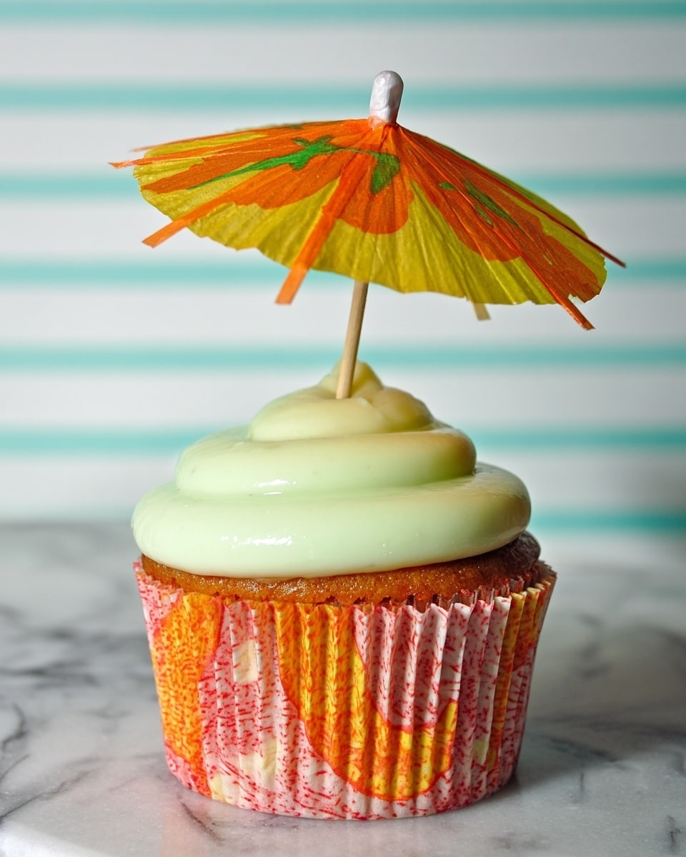 A single cupcake with a colorful, orange and red patterned liner sits in the center. The cupcake is topped with a smooth, light green frosting layer that looks creamy and soft. A small paper umbrella with orange and yellow colors is placed upright in the frosting, adding a fun, tropical touch. The cupcake rests on a white marbled surface with a soft, striped white background behind it. photo taken with an iphone --ar 4:5 --v 7