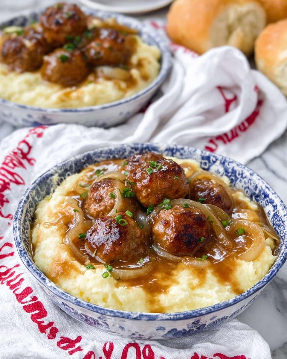 The image shows two white bowls with blue patterns filled with mashed potatoes and brown meatballs on top. The mashed potatoes layer is creamy and light yellow, covering the bottom of the bowl. On top, several round, browned meatballs sit, covered in a glossy brown onion gravy with visible thin slices of cooked onions and small green herb bits sprinkled over. The bowls are placed on a white cloth with red text, set on a white marbled surface, and there are pieces of soft bread rolls around. Photo taken with an iphone --ar 4:5 --v 7