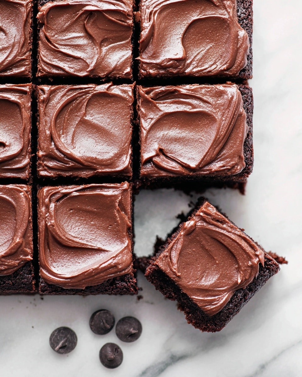 A close-up view of a chocolate brownie cut into 12 square pieces arranged in a 4x3 grid on a white marbled surface. Each brownie piece has a thick layer of smooth, glossy chocolate frosting with soft swirls on top, showing a rich, deep brown color. One brownie is slightly pulled out from the grid and positioned at the bottom left with clear edges, highlighting the moist and dense texture underneath the frosting. Three chocolate chips are placed near the bottom center of the image on the white marbled surface. The photo taken with an iphone --ar 4:5 --v 7