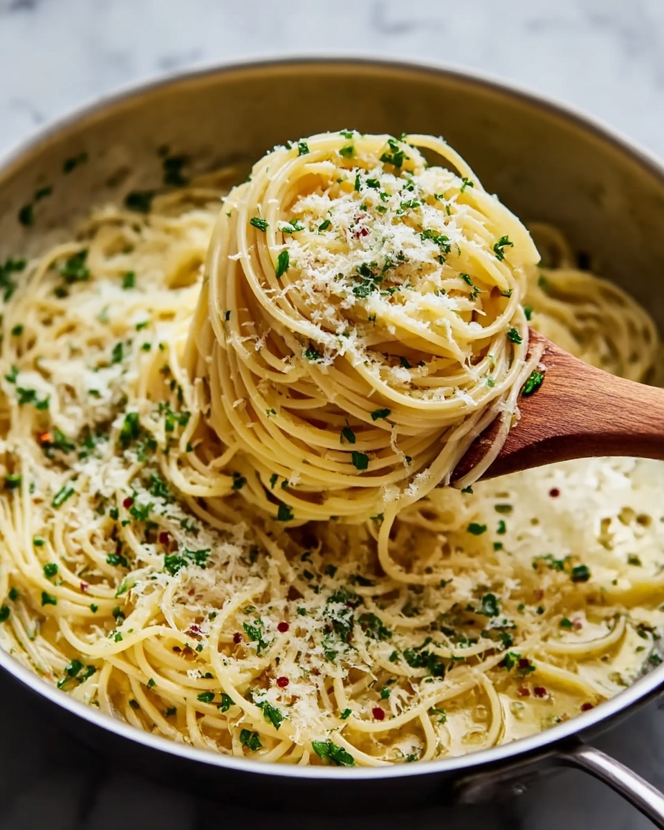 A close-up view of a pan filled with cooked spaghetti pasta, where a wooden spoon is lifting a neat bundle of spaghetti strands twisted around it. The pasta is coated lightly in a shiny, golden oil-based sauce. It is topped with small green bits of fresh herbs and a sprinkling of grated white cheese, with tiny red pepper flakes scattered throughout. The pan sits on a white marbled surface, and the overall look is warm and inviting, showing the texture of the noodles clearly. Photo taken with an iphone --ar 4:5 --v 7