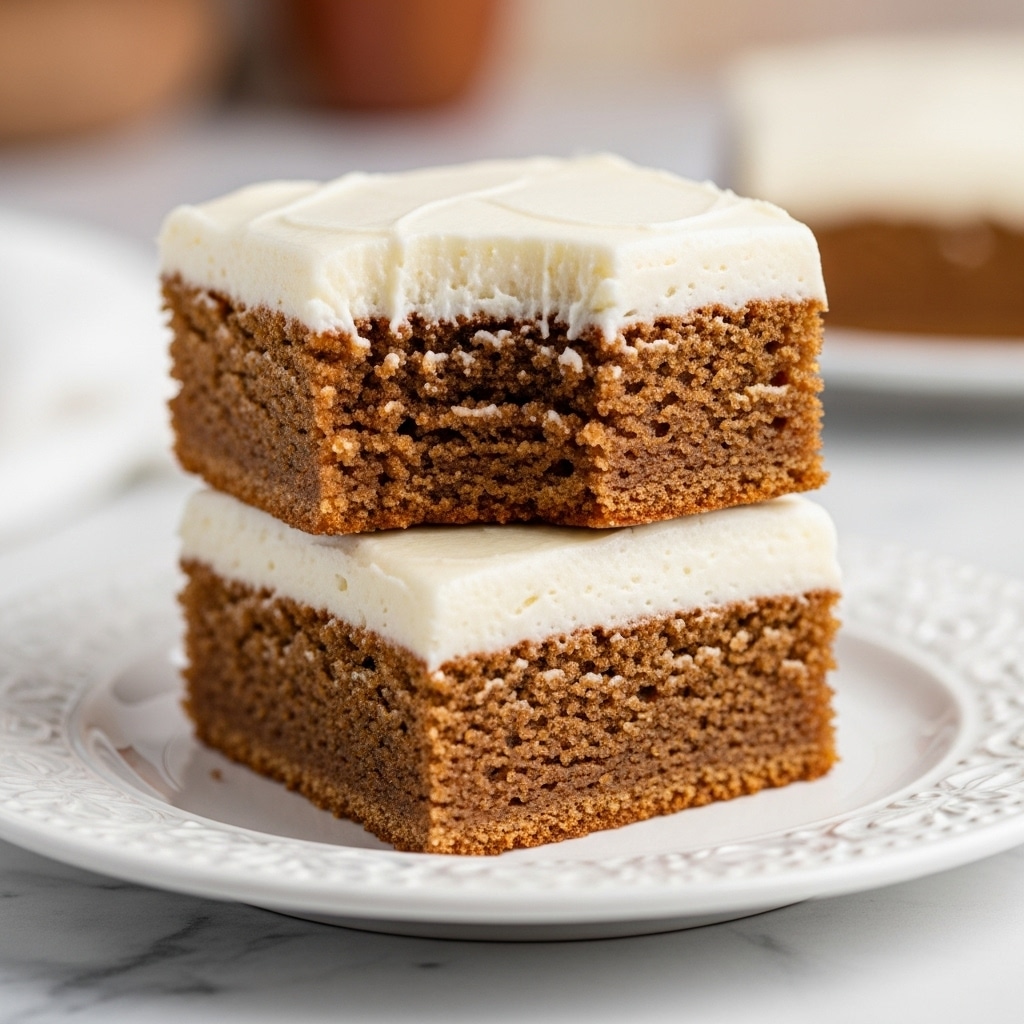 The image shows two square pieces of light brown cake stacked on a white plate with delicate small crumbs around. Each cake piece has a smooth, thick layer of white frosting on top. The top piece has a bite taken out, revealing the soft, moist texture inside. The background is a white marbled surface with blurred warm-toned elements in the back. Photo taken with an iphone --ar 4:5 --v 7