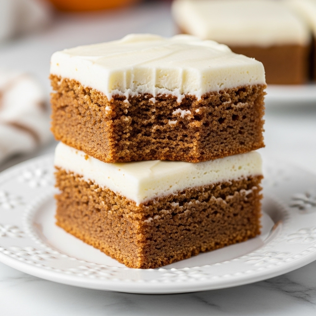 Two square pieces of cake stacked on a white plate with small decorative details around the edges. Each cake piece has two layers: a moist, brown gingerbread base with a slightly crumbly texture, topped with a thick, smooth layer of creamy white frosting. The top piece has a bite taken out of one corner, showing the soft inside of the cake. The background is a soft blur hinting at warm colors, all set on a white marbled surface. Photo taken with an iphone --ar 4:5 --v 7