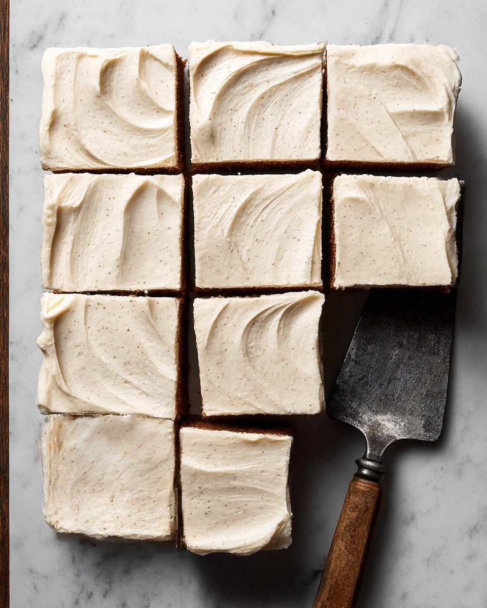 A square cake is cut into nine equal pieces arranged in a 3x3 layout on a white marbled surface. Each piece has two visible layers: a thick bottom layer of moist, dark brown cake, topped with a thick, smooth layer of creamy off-white frosting with fine specks, spread evenly with soft curls and waves. The cake edges are clean and crisp with some frosting slightly overlapping the sides. A metal spatula with a rustic handle lies beside the cake on the white marbled surface. photo taken with an iphone --ar 4:5 --v 7
