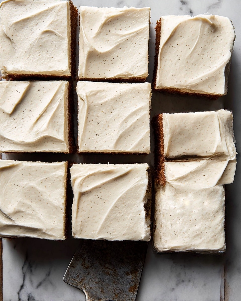 A square cake cut into nine pieces sits on a white marbled textured surface, each piece topped with a thick, creamy layer of light beige frosting with soft swirls and slight specks giving it a textured look. The cake underneath is a warm brown color, visible around the edges and in between the pieces. The frosting is evenly spread with gentle peaks and waves, showing the smooth yet fluffy texture on the top and sides of each square. A metal cake server with a slightly worn look rests beside the cake. The overall setting has a cozy and rustic feel. photo taken with an iphone --ar 4:5 --v 7