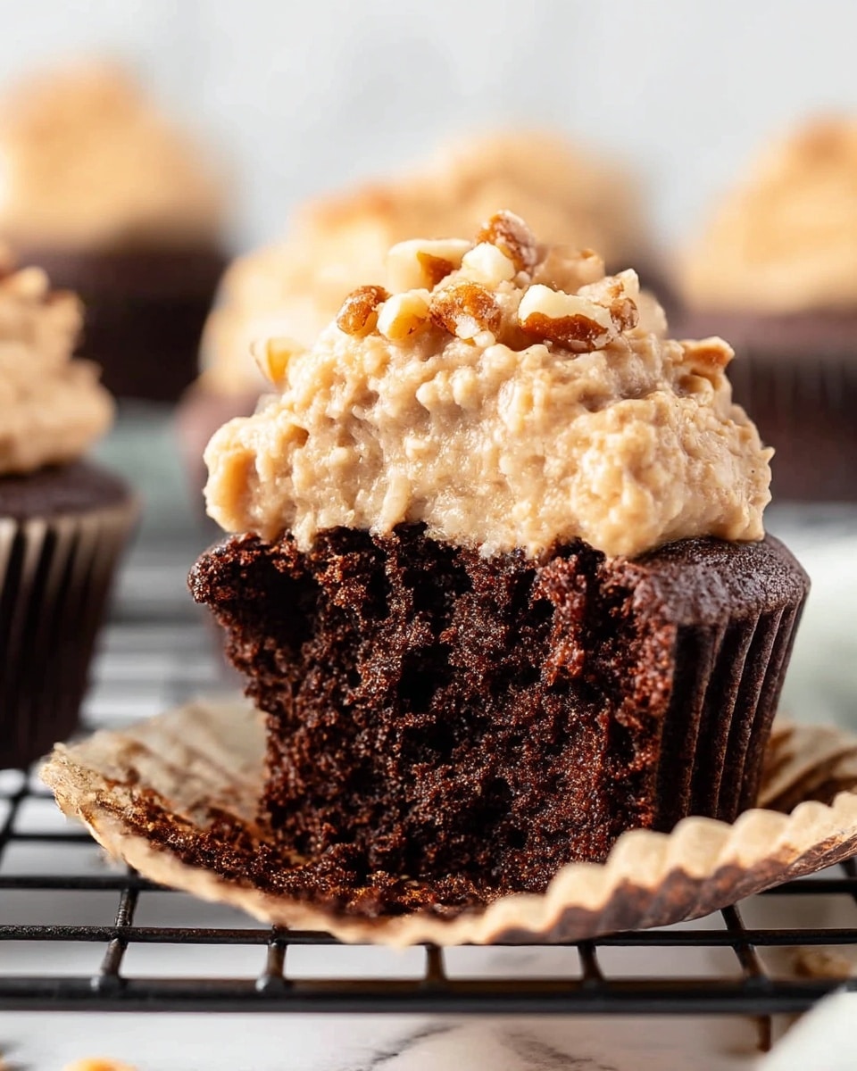 A close-up of a chocolate cupcake with two layers: the bottom layer is dark and moist with a rich chocolate texture, and the top layer is thick, creamy frosting in a light tan color mixed with small chopped nuts, giving it a chunky texture. The frosting covers the whole top of the cupcake with some nuts sprinkled on top. The cupcake is placed on a white marbled texture surface with blurred cupcakes in the background. Photo taken with an iphone --ar 4:5 --v 7